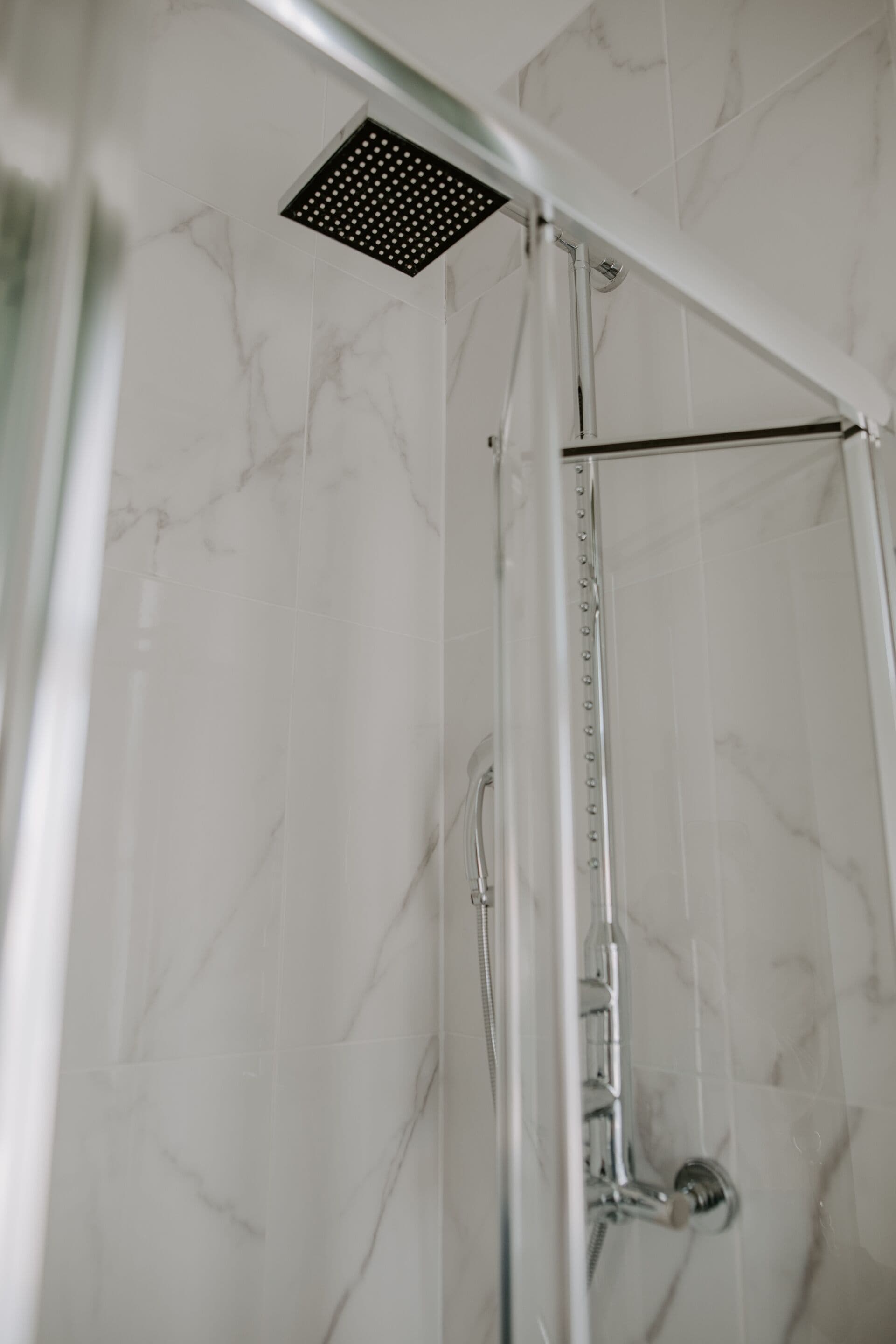 A shower with a square ceiling-mounted showerhead, a vertical water control panel, and a metal shower hose.