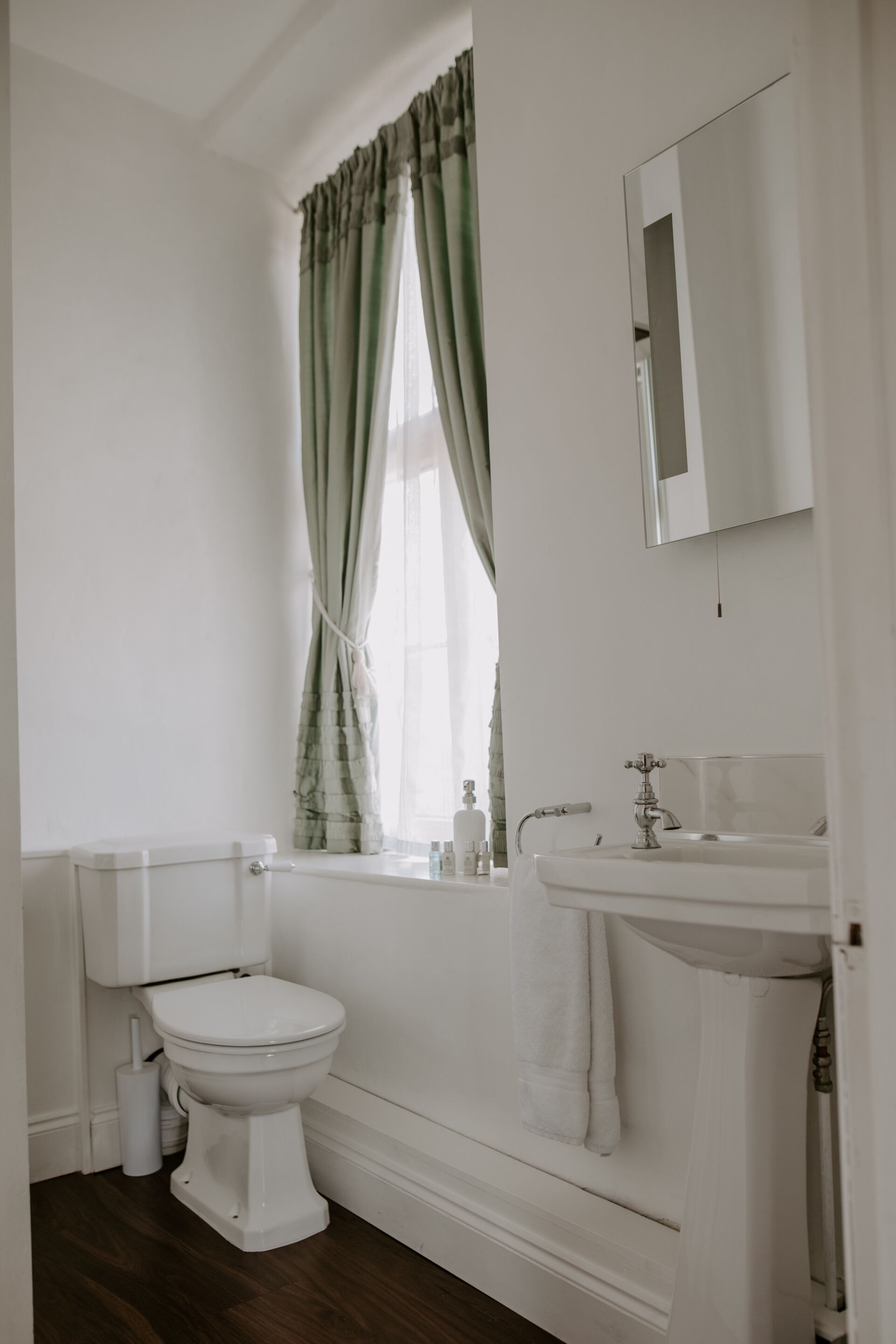 A bathroom with a toilet, sink, and window with curtains.