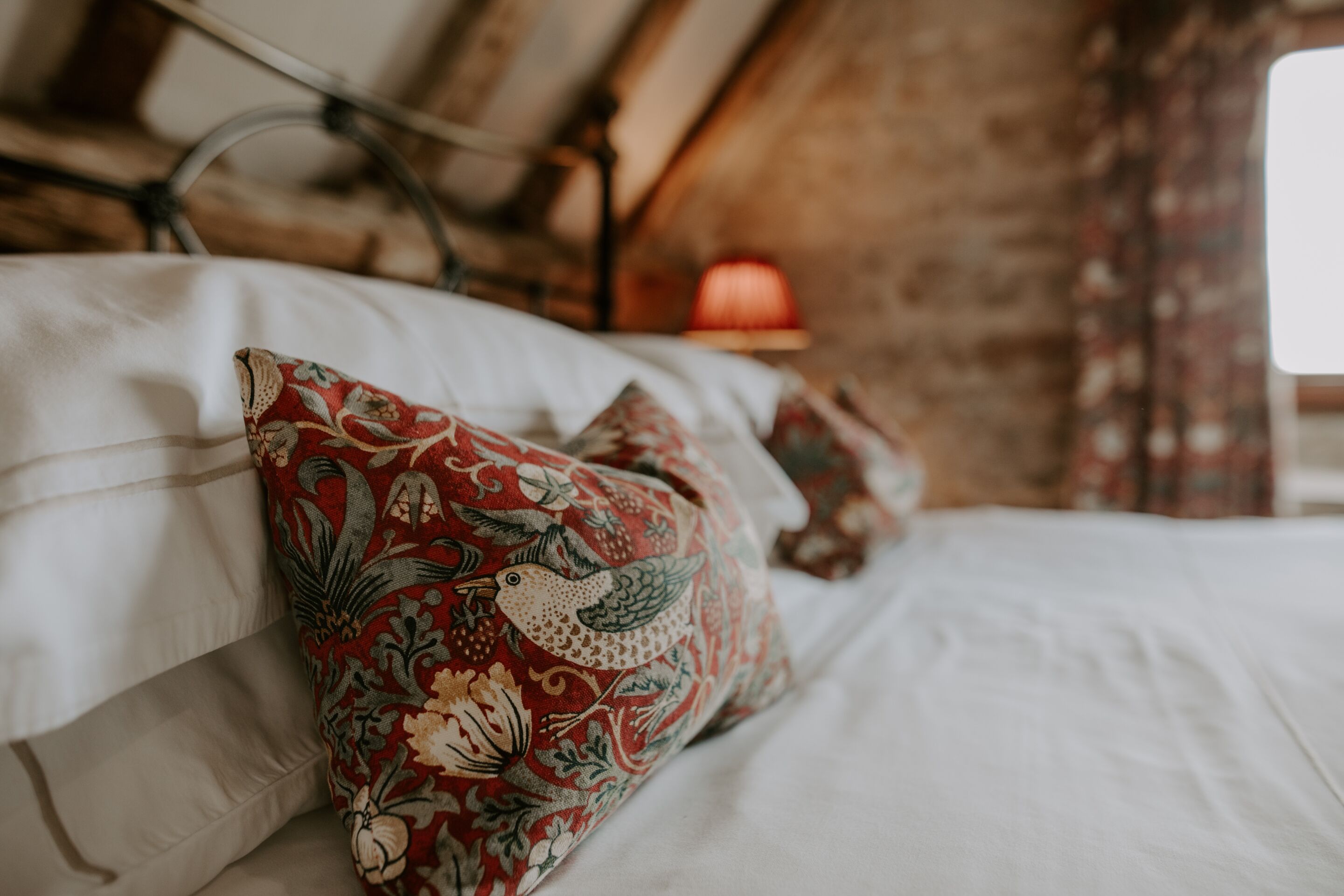 Un letto con cuscini decorati, una testiera in legno e una lampada rossa su un comodino.