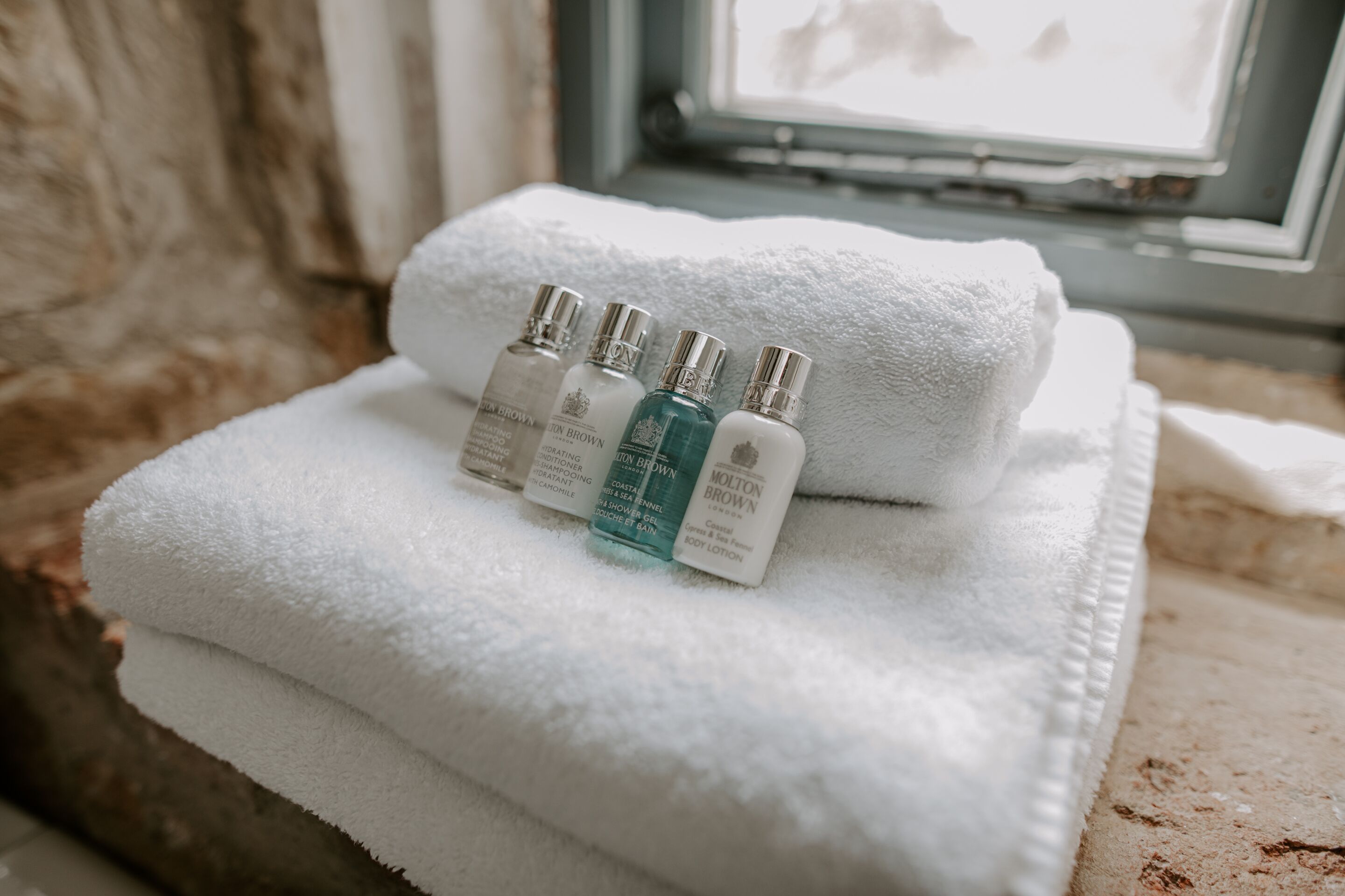 A stack of white towels with three bottles of lotion on top.
