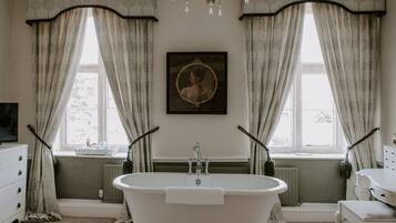 A bathroom with a freestanding bathtub, a radiator, a framed portrait, and a window with curtains.