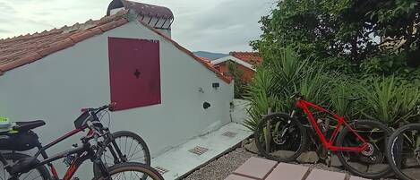 A white building with a red door, a red bicycle, and a red bicycle parked on a tiled patio.