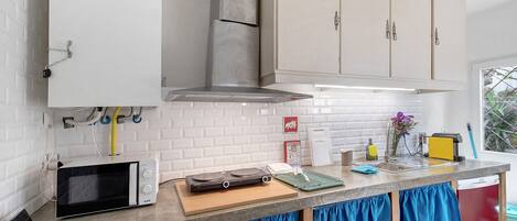 A kitchen with a microwave, toaster, and a small countertop with a cutting board and a green mat.