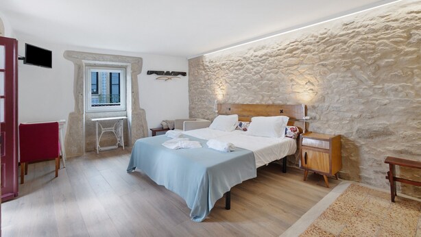 Een slaapkamer met een stenen muur, een bed met witte lakens, een houten nachtkastje, een rode stoel en een kleine tafel.