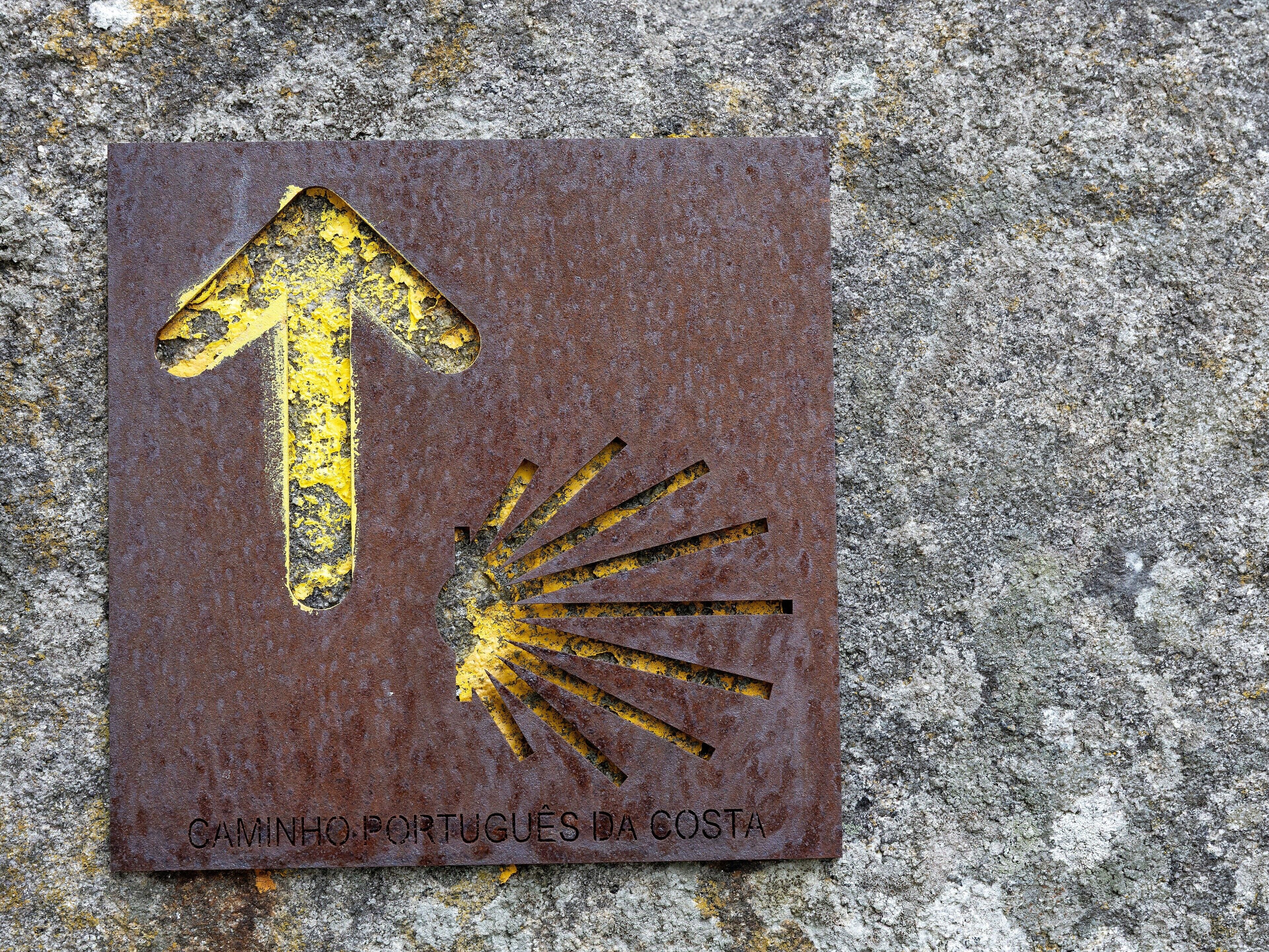 Een verweerd metalen bord met een pijl en zon ontwerp, bevestigd aan een structuurrijk stenen oppervlak.