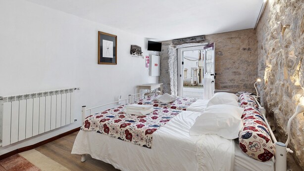 Un dormitorio con cama, paredes blancas, radiador y pared de piedra.