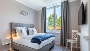 A bedroom with a bed, a window, a chair, and a TV. - Seaside Comfort Travemunde Stay (Lübeck)