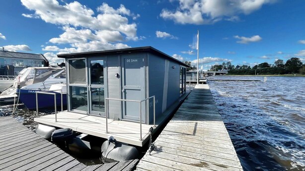 A stationary boat with a cabin, docked on a wooden pier, with a clear sky and calm water in the background. - Houseboat for 4 on Uitgeester Lake (Uitgeest)