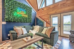 A cozy living room with a green sofa, a wooden coffee table, and a neon sign on the wall.