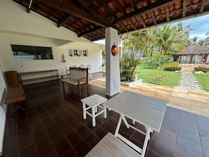 An outdoor patio with a wooden bench, a white table, and a thatched-roof structure.