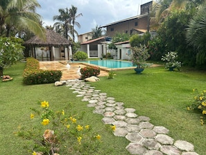 A backyard with a swimming pool, a thatched-roof structure, and a stone pathway.