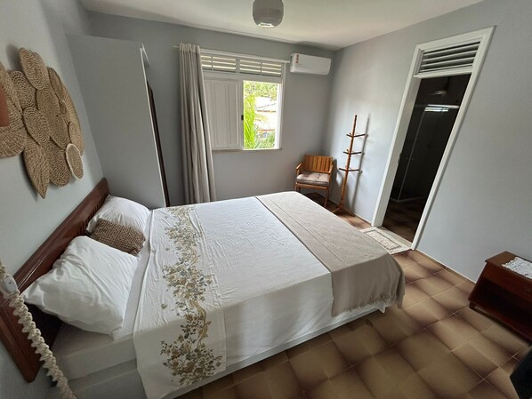 A bedroom with a bed, a chair, a coat rack, and a window with curtains.