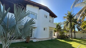 A white two-story house with a sloped roof, a well-maintained lawn, and several palm trees. - Prainha - Aquiraz 5-bedroom summer mansion (Aquiraz)