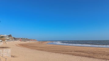 Una playa con cielo despejado, orilla arenosa y algunos edificios al fondo.