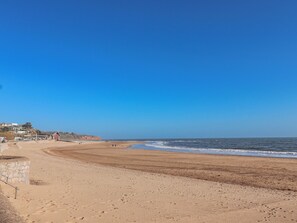 A beach with a clear sky, sandy shore, and a few buildings in the background. - Sea Lovers (Exmouth)