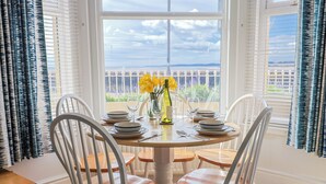 Una mesa de comedor con sillas blancas, un jarrón con flores amarillas y una botella de vino.