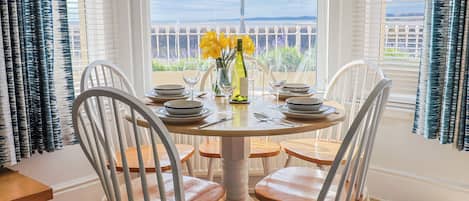 A dining table with white chairs, a vase with yellow flowers, and a bottle of wine.