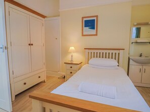 A bedroom with a bed, a nightstand with a lamp, a wardrobe, a bathroom with a sink, and a framed picture on the wall. - Sea Lovers (Exmouth)