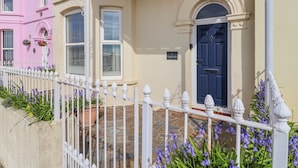 A two-story building with a white picket fence, a blue door, and a stone-paved entrance. - Sea Lovers (Exmouth)