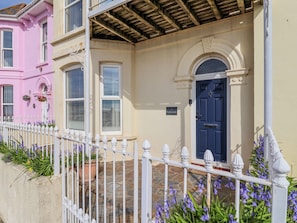 A two-story building with a white picket fence, a blue door, and a stone-paved entrance. - Sea Lovers (Exmouth)