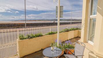 Un balcón con mesa y sillas, vista al mar y una valla blanca.