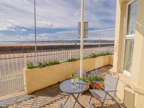 A balcony with a table and chairs, a view of the sea, and a white fence. - Sea Lovers (Exmouth)