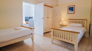 A bedroom with two beds, a wardrobe, a bedside table with a lamp, and a framed picture on the wall. - Sea Lovers (Exmouth)