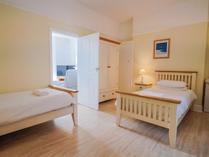 A bedroom with two beds, a wardrobe, a bedside table with a lamp, and a framed picture on the wall. - Sea Lovers (Exmouth)