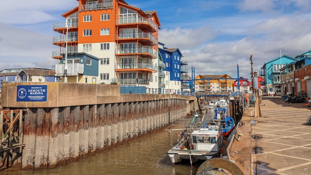 A waterfront marina with multi-story buildings, a boat docked at the pier, and a sign indicating it's for berth holders only. - Sea Lovers (Exmouth)