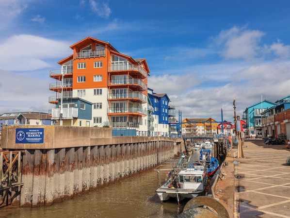 A waterfront marina with multi-story buildings, a boat docked at the pier, and a sign indicating it's for berth holders only. - Sea Lovers (Exmouth)