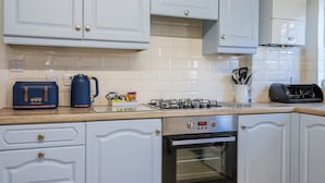 A kitchen with white cabinets, a stove, an oven, a coffee maker, and a toaster. - Sea Lovers (Exmouth)