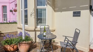 A patio with a table and chairs, a bottle of wine, and potted plants. - Sea Lovers (Exmouth)