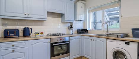 A modern kitchen with white cabinets, a built-in oven, a washing machine, and a window with a view.