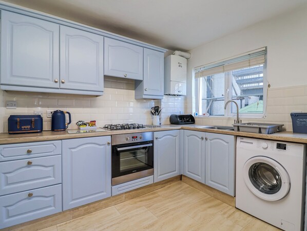 A modern kitchen with white cabinets, a built-in oven, a washing machine, and a window with a view.