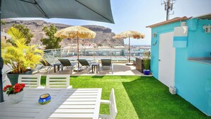 Un patio con mobiliario exterior, una mesa con un jarrón de flores y vistas a un paisaje montañoso.