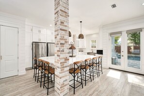 A modern kitchen with white cabinets, a brick column, and a bar area with stools. - Waterdog I | Private Pool/Spa | Game Room | Golf Cart | Walk to Beach (Destin)