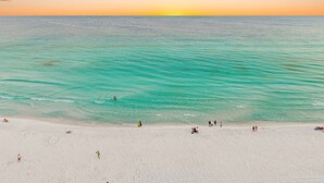 Ein Strand mit klarem türkisblauem Wasser, einem sandigen Ufer und einem Sonnenuntergang im Hintergrund.