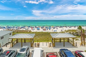 A beach view with a parking area, beach umbrellas, and beachgoers. - Waterdog II | Community Pool/Hot Tub | Tram to Beach (Destin)