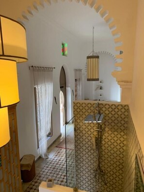 A bathroom with a patterned shower wall, a hanging light fixture, and a visible shower control.