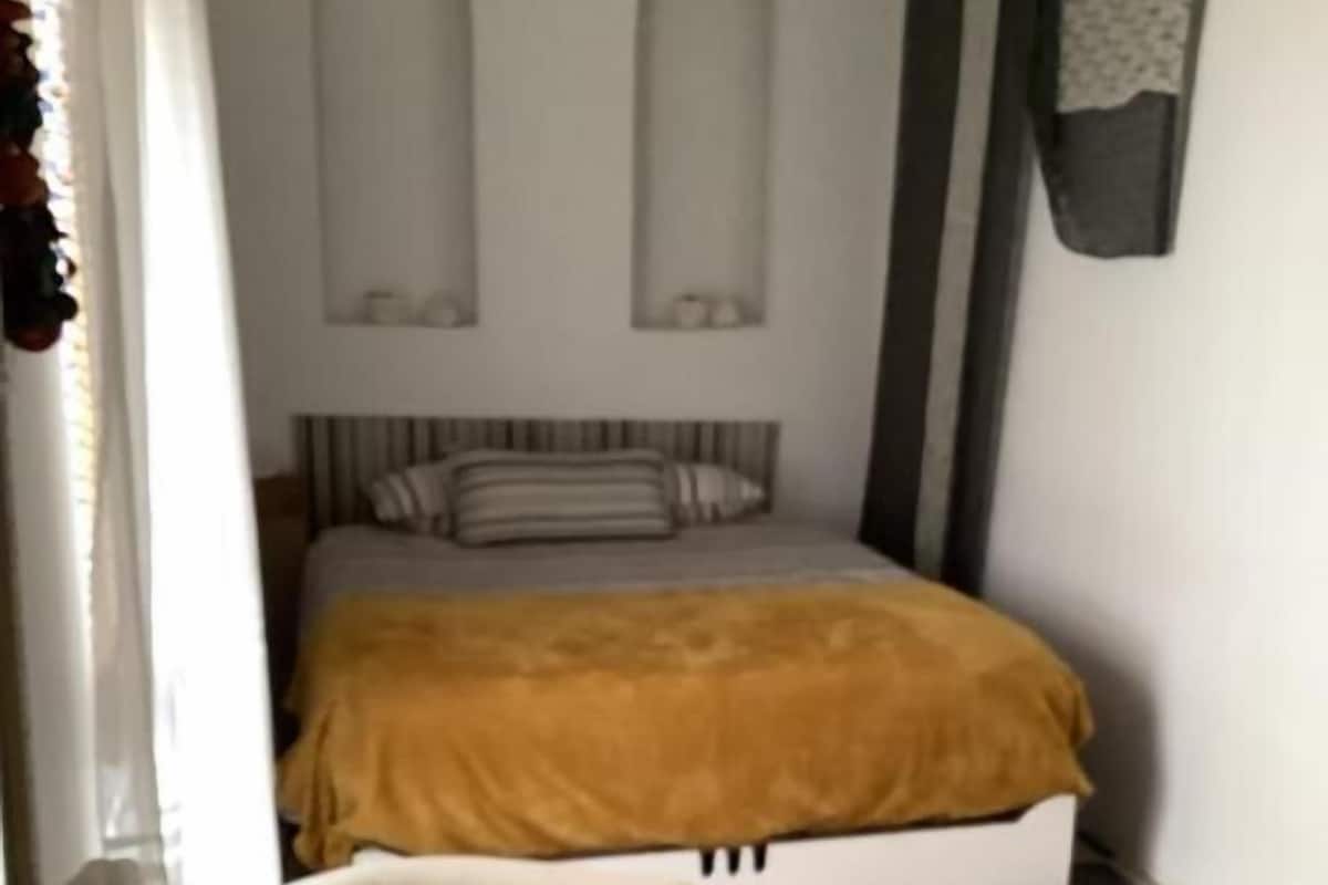 A bedroom with a bed, a white chair, a vase with flowers, and a patterned rug.