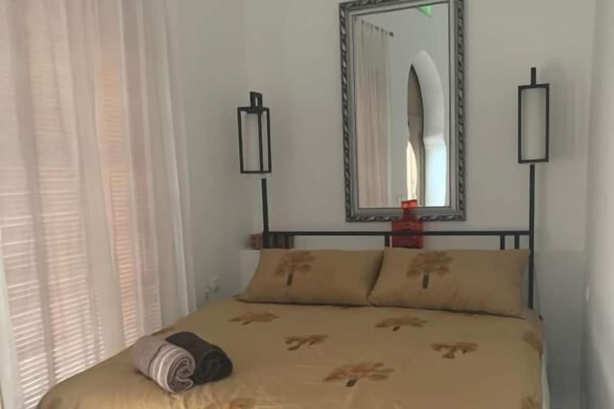 A bed with a floral bedspread, a mirror above it, and two wall-mounted lamps.
