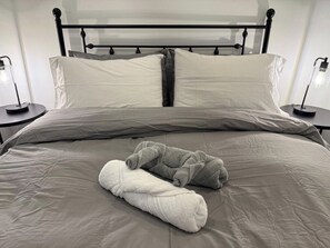 Een bed met een grijze dekbedovertrek, twee kussens en twee opgerolde handdoeken.