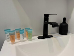 Een wastafel met een zwarte kraan, een zeepdispenser en vijf flesjes lotion.