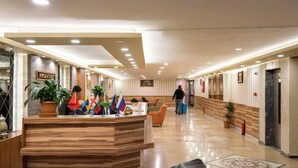 A hotel reception area with a wooden reception desk, multiple flags, and a person walking in the background. - Dınar Hotel (Istanbul)