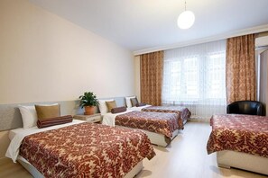 Une chambre d’hôtel avec trois lits, une plante en pot et une vue sur les immeubles par la fenêtre.