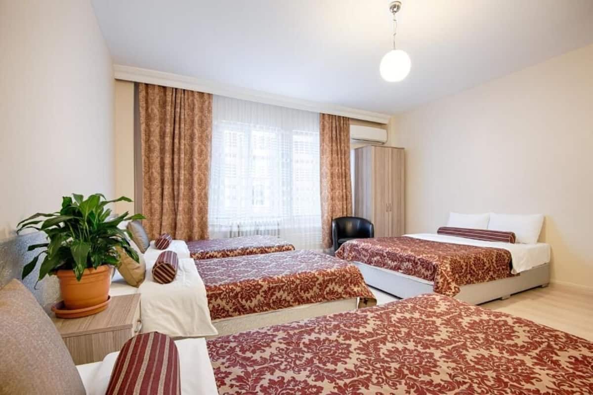 Habitación de hotel con tres camas, una planta en maceta y una lámpara en el techo.