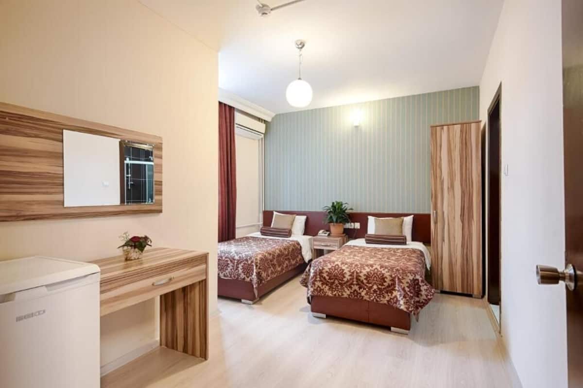 Habitación de hotel con dos camas, un escritorio, un refrigerador y un espejo.