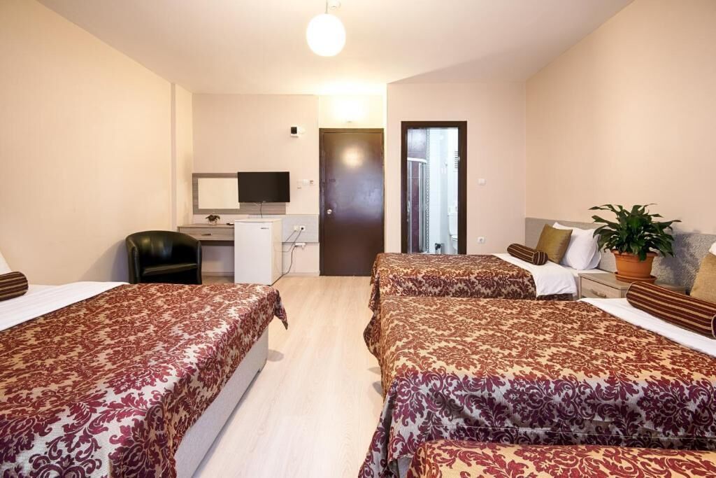 A hotel room with two beds, a desk, a chair, a television, and a door leading to a balcony.