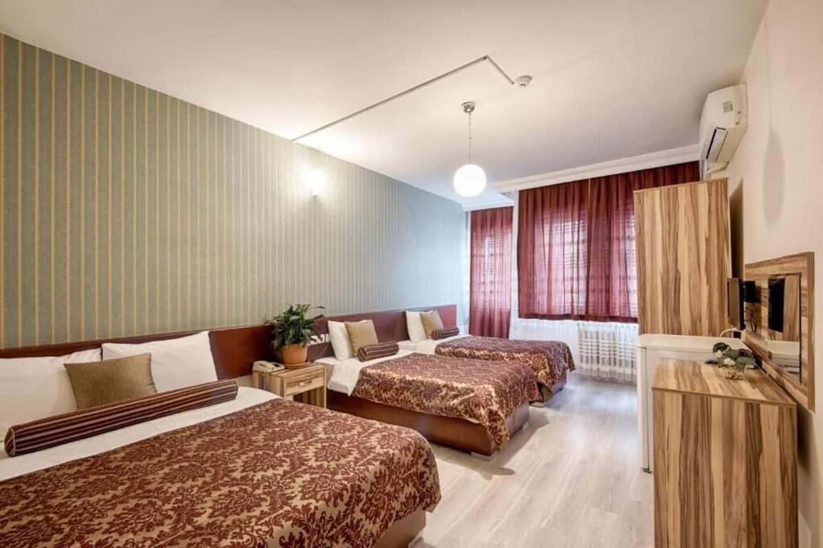 Una habitación de hotel con tres camas, televisión, escritorio y ventana con cortinas.