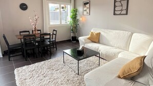 A living room with a sofa, coffee table, dining table, chairs, a potted plant, and artwork on the walls. - Modern house with terrace and parking. Overlooking the city (Clermont-Ferrand)